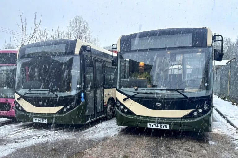 Two Alexander Dennis Enviro200 buses stand side by side in the falling snow.