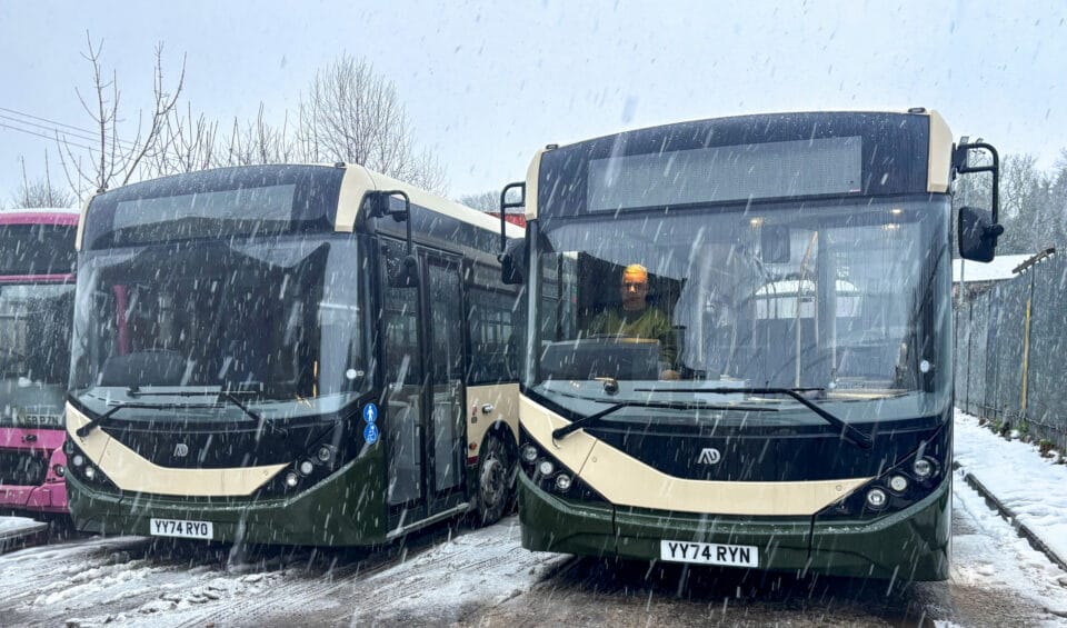 Two Alexander Dennis Enviro200 buses stand side by side in the falling snow.