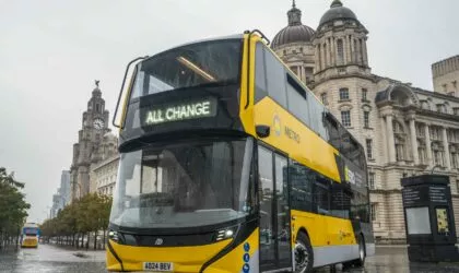 An Alexander Dennis Enviro400EV in the colours of the Liverpool City Region's Metro network stands in front of the Three Graces buildings on Liverpool's Pier Head.